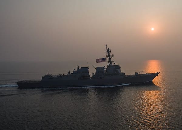 A Navy ship underway, heading into the sunset.